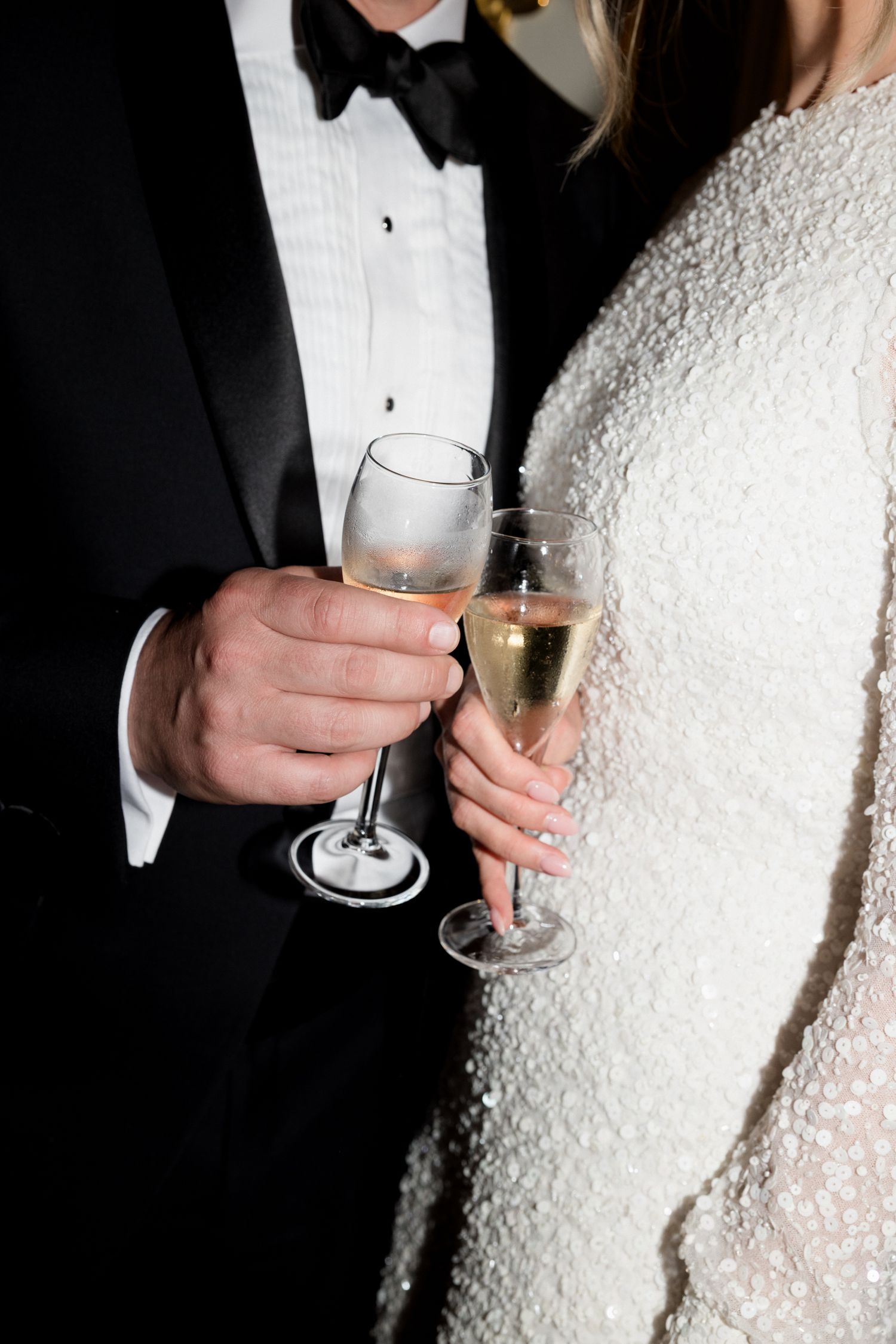 Close-up of hands holding champagne glasses at a formal wedding celebration in black and white. editorial wedding france photographer