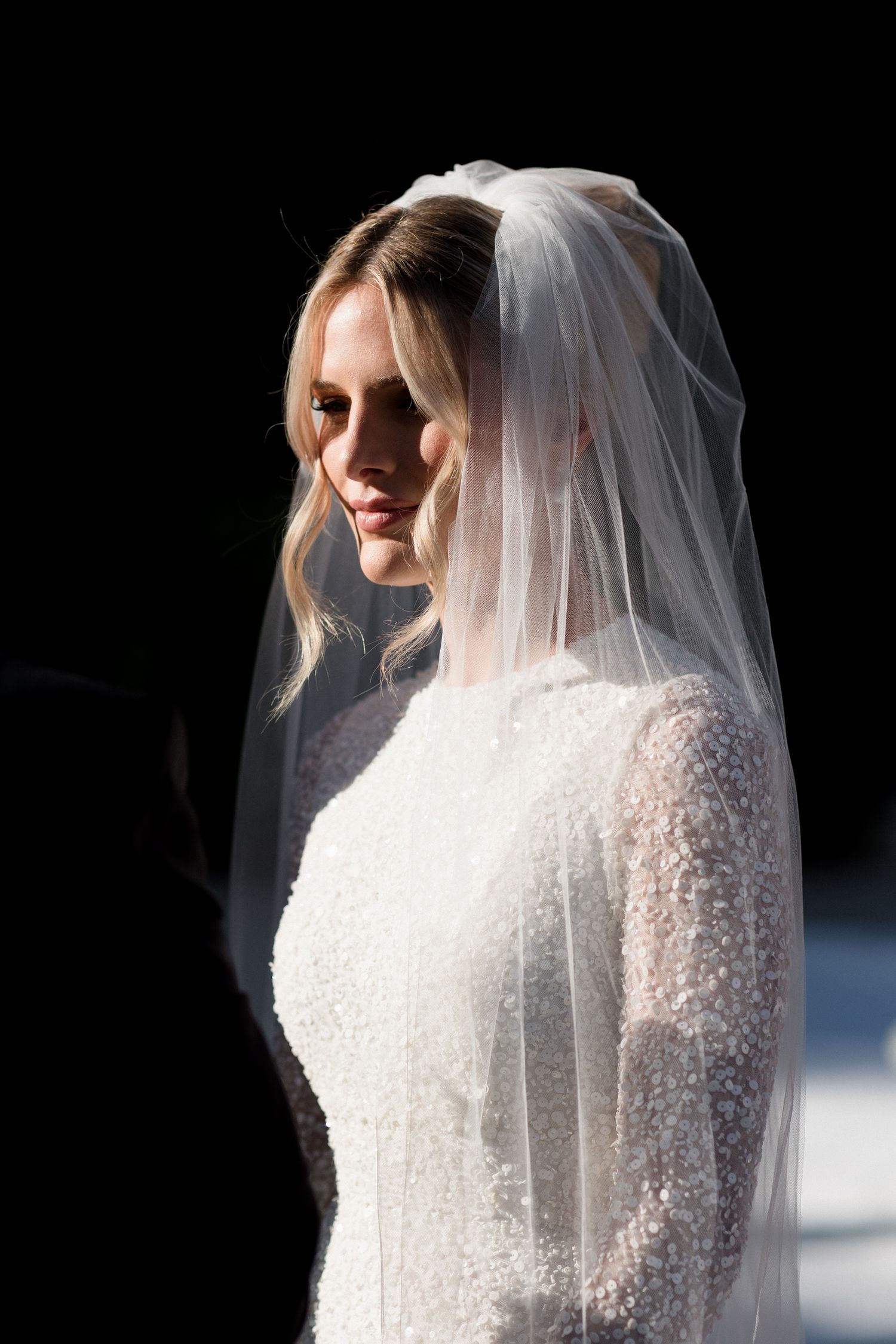 A bride in a long-sleeved lace wedding gown and flowing veil poses against a dark background in a series of shots. editorial wedding photog