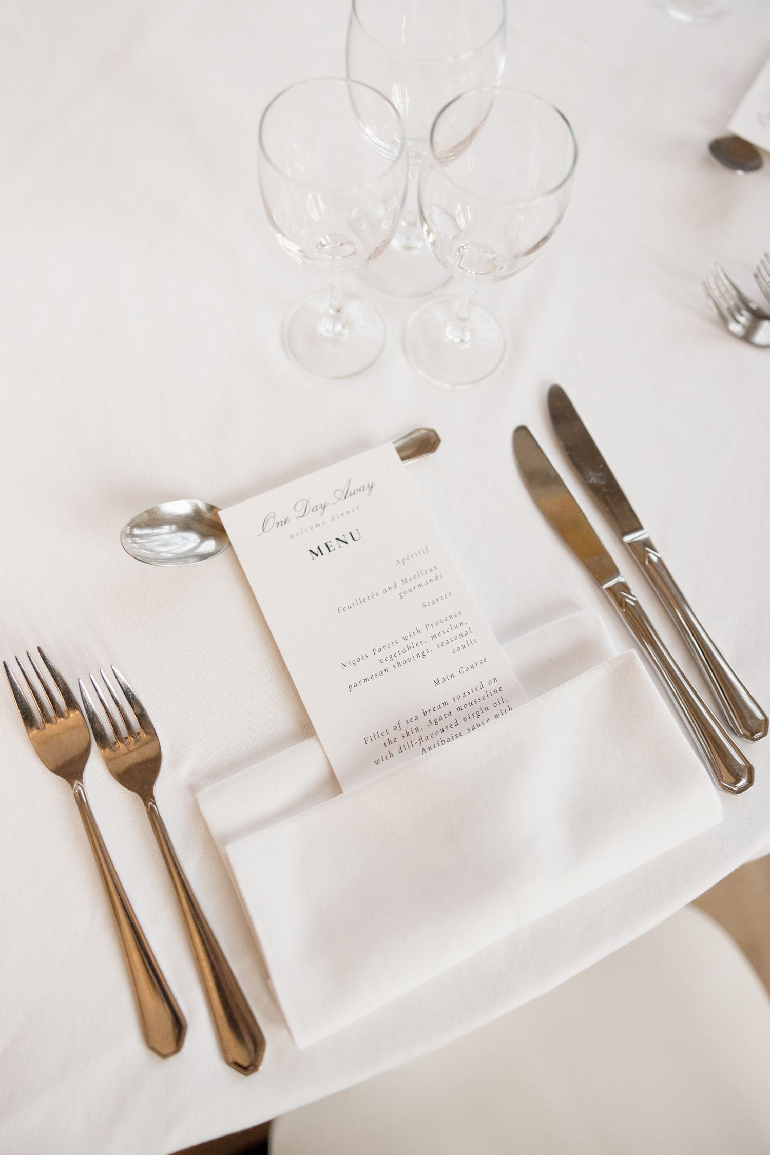 Elegant table setting with white linens, silverware, and menu cards in a minimalist style.
