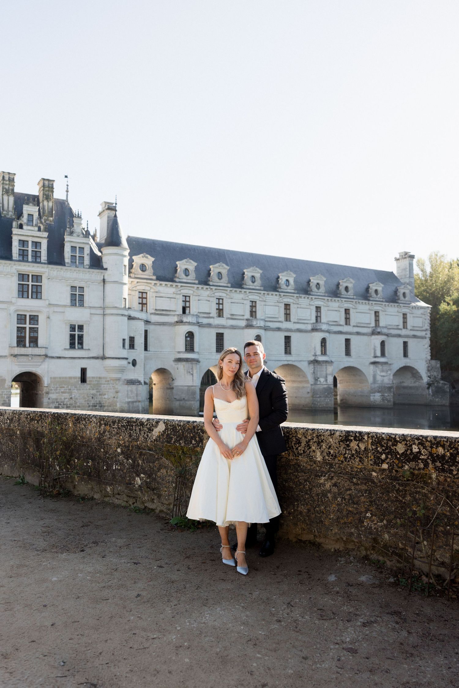Bride and groom posing before Château de Chenonceau spanning the River Cher in the Loire Valley, France.