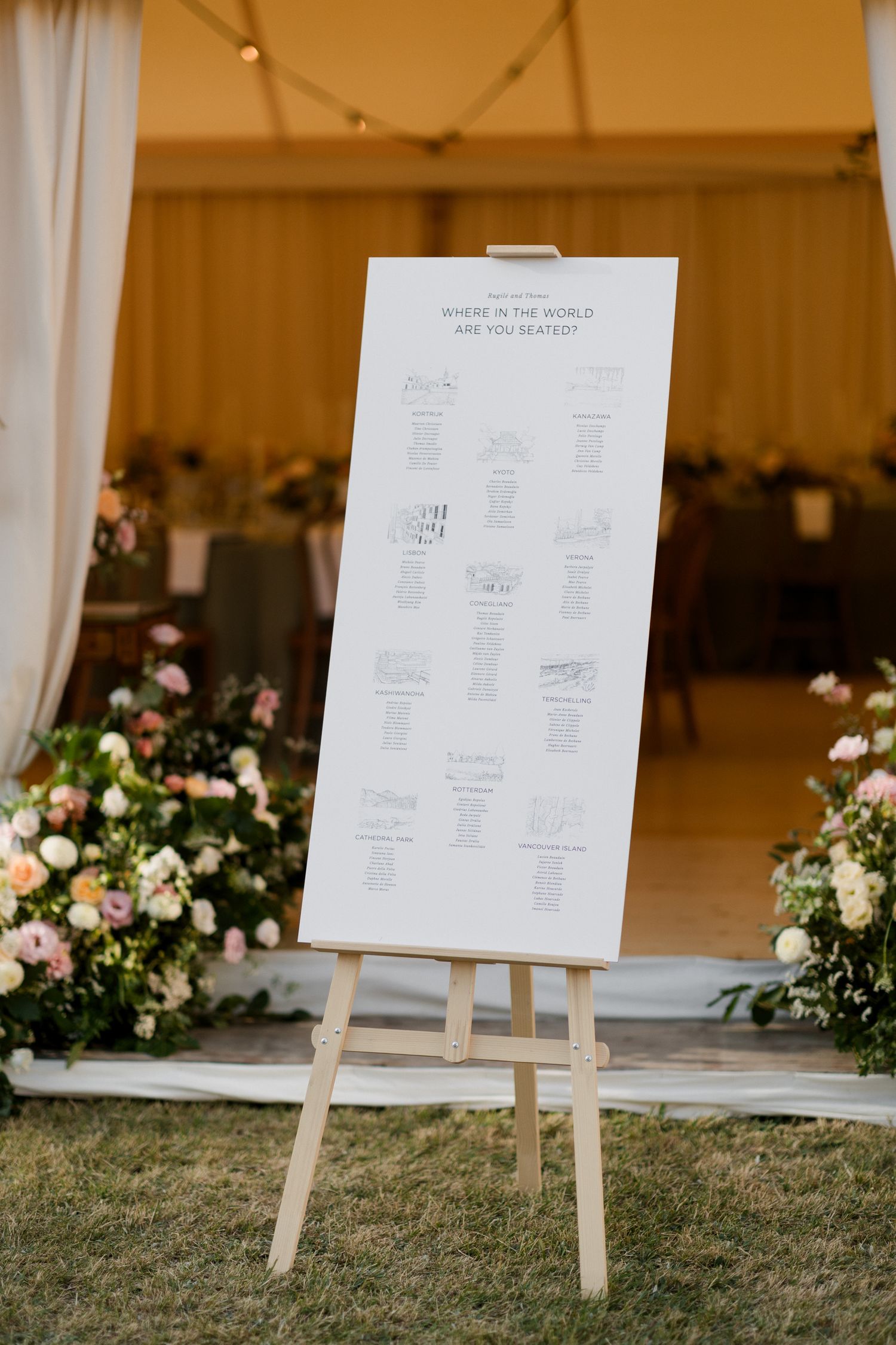 Wedding seating chart displayed on wooden easels with floral arrangements decorating the outdoor venue.