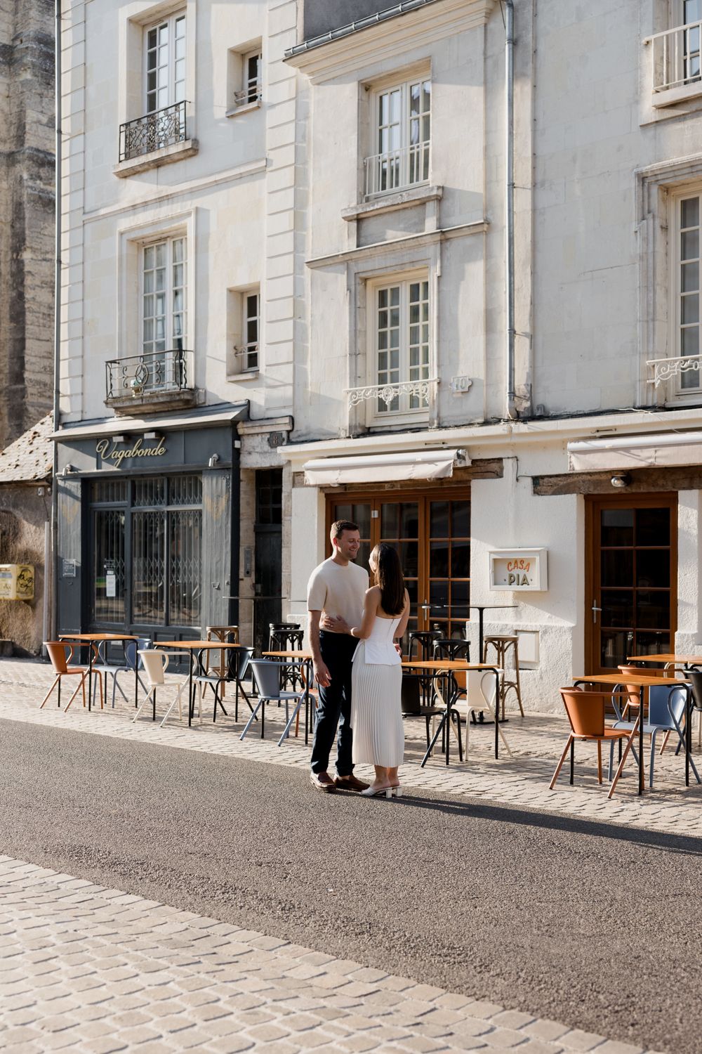 White stone buildings with cafes and shops along a cobblestone street in a charming European city.