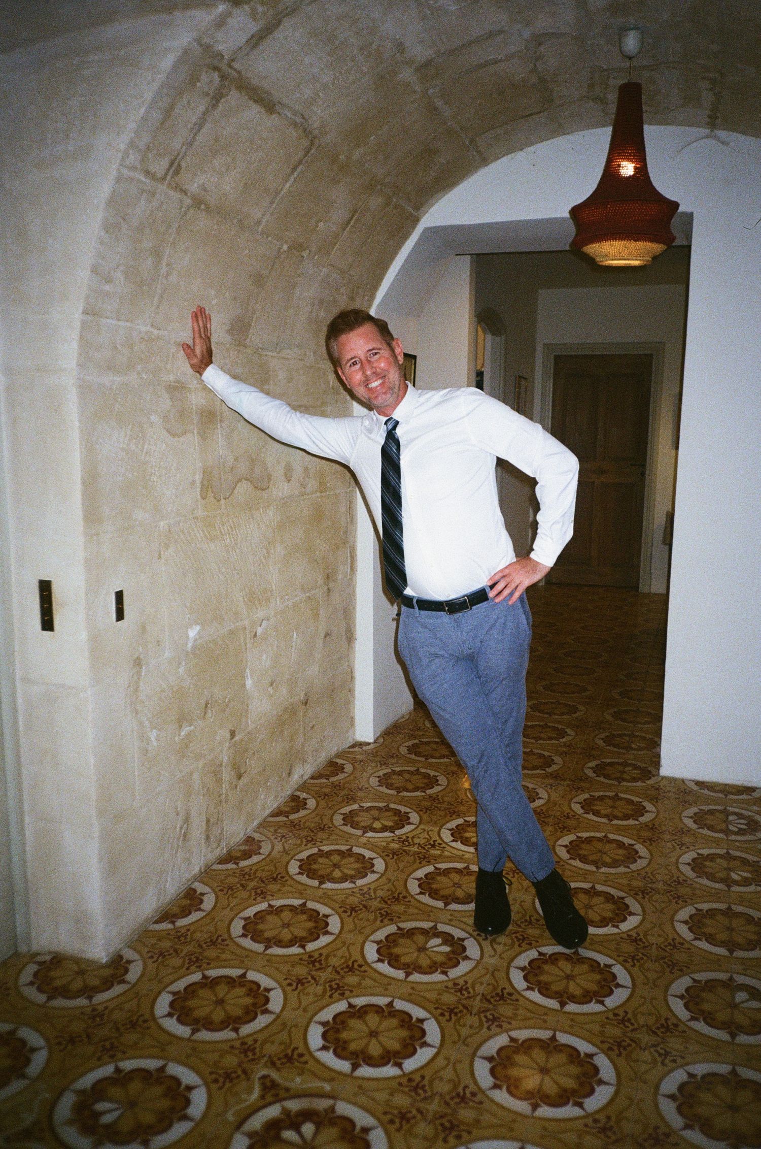 Person examining vintage patterned carpet in dimly lit hallway with stone walls showing progression of movement.
