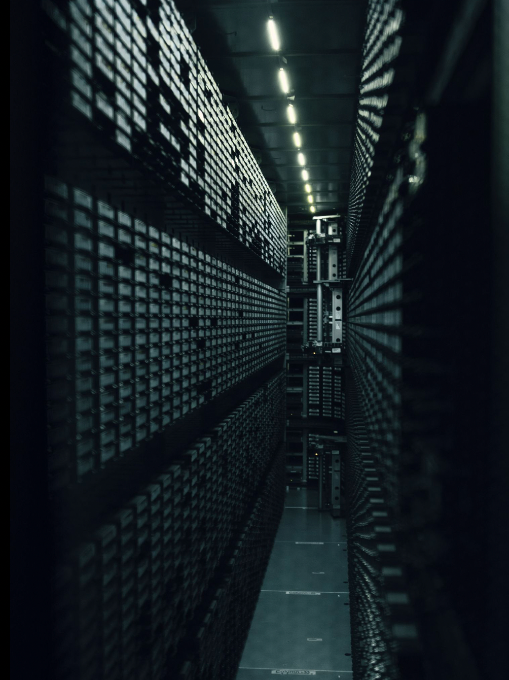 Dark corridor with rows of metal grid storage units and fluorescent lighting creates an industrial mood.