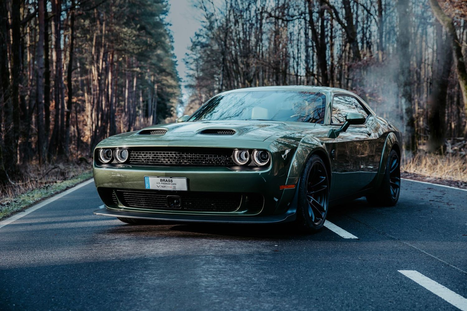 A black Dodge Challenger Hellcat with glowing headlights sits menacingly on a misty forest road.