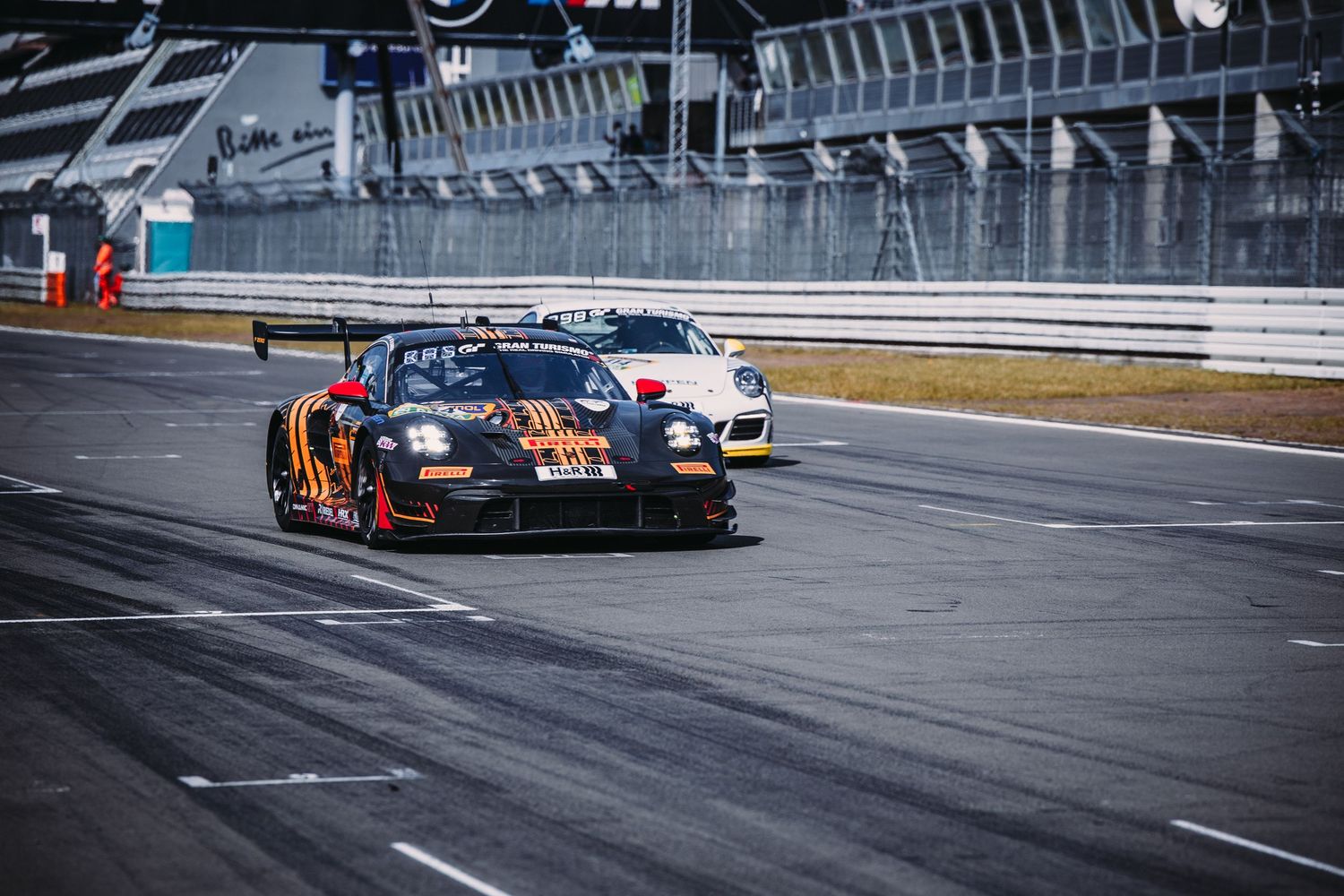 Racing car with distinctive orange and black livery speeds around a professional motorsport track during competition.