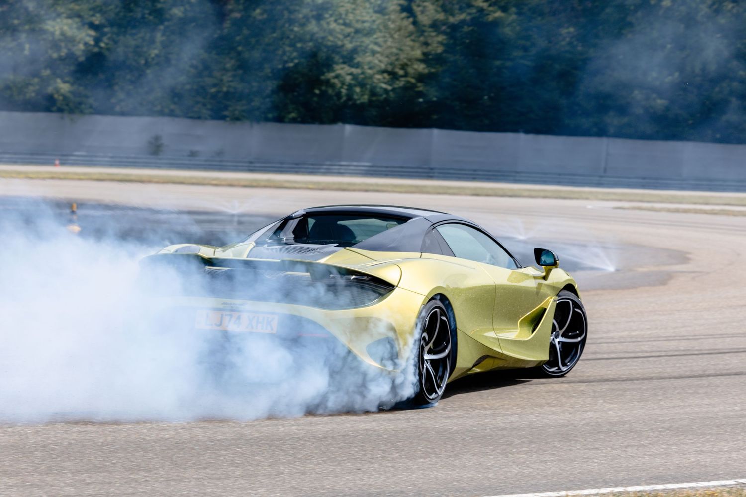 Yellow McLaren supercar drifting on racetrack with smoking tires during high performance driving.