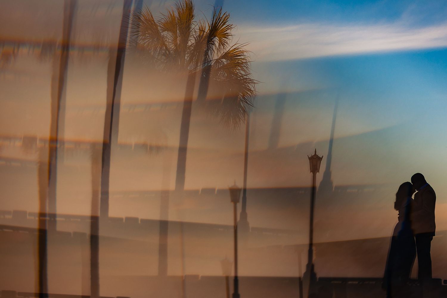 Romantic couple silhouetted at sunset with palm trees reflected on glass wall at beach promenade.
Charleston, SC