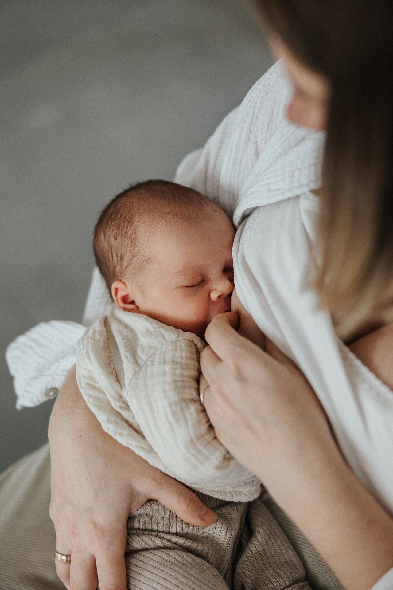 A tender moment of breastfeeding as a baby in white clothing nurses while being cradled in loving arms.