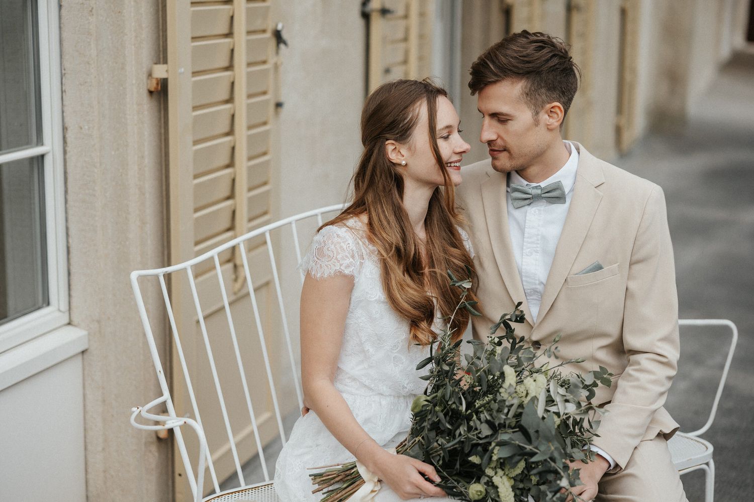 Romantic wedding couple embraces on a veranda with white chairs in the background.