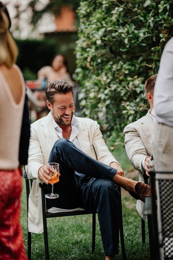 Gast im weißen Blazer und dunkelblauer Hose entspannt auf einem Stuhl bei einer Gartenparty – elegant heiraten im Morrhof.