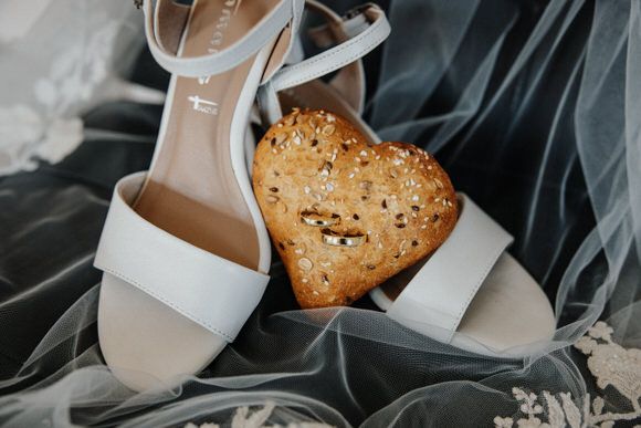 White wedding heels and gold jewelry arranged on dark fabric with scattered gold confetti details.