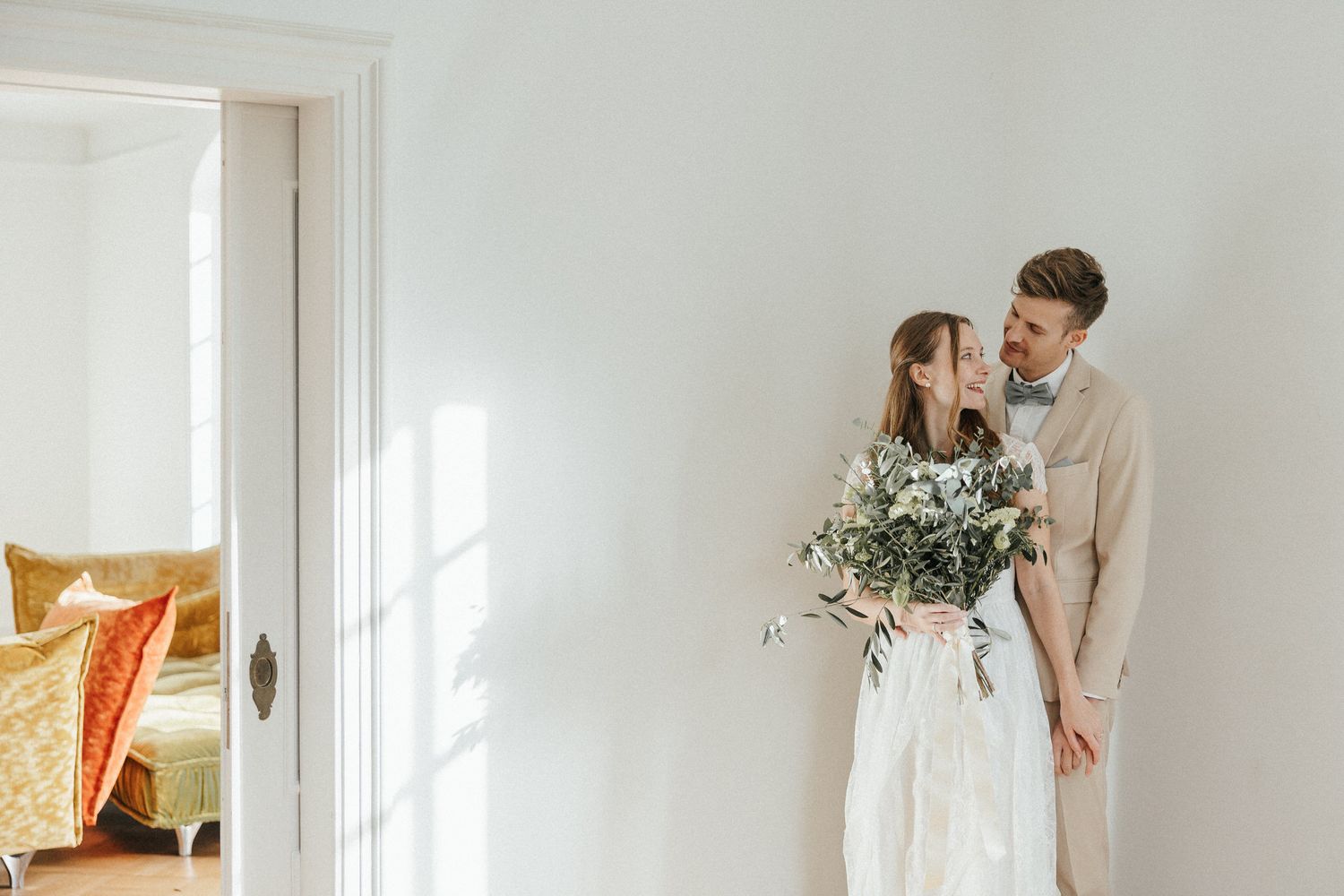 An intimate wedding moment captured in a bright white room with natural window light.