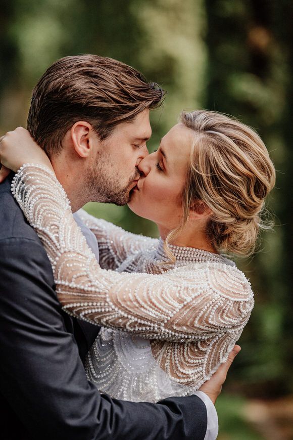 Nahaufnahme eines romantischen Hochzeitskusses mit feinen Spitzenärmeln – Liebe pur beim heiraten im Morrhof.