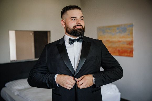 A groom adjusts his black suit jacket while getting ready for a wedding ceremony.