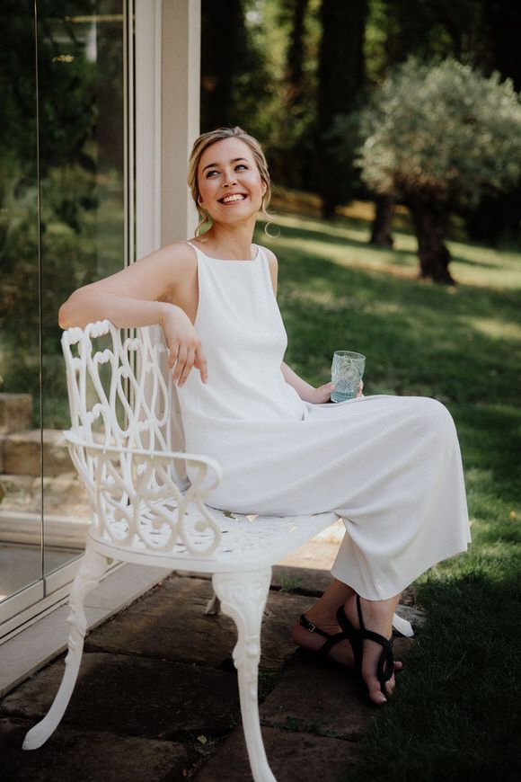 Person im weißen Kleid entspannt auf kunstvoller weißer Bank auf sonniger Veranda – elegant heiraten im Morrhof.