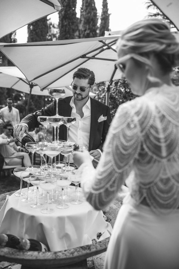 Schwarz-Weiß-Aufnahme von Gästen, die beim Einschenken des Champagnerturms zuschauen – exklusiv heiraten im Morrhof.