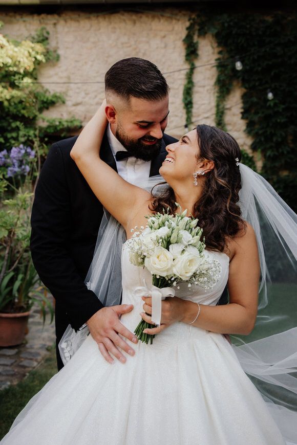 Elegant bride and groom share an intimate moment in a garden setting with white floral bouquet.