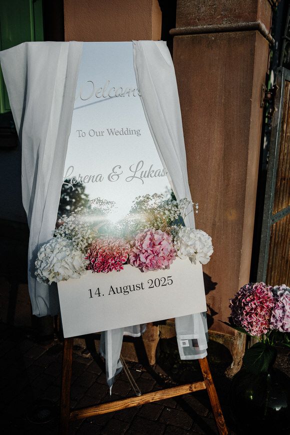 Hochzeitsfotograf Boudier & Koeller – Hochzeits-Willkommensschild mit getrockneten Blumen und weißem Tüll auf Holz.