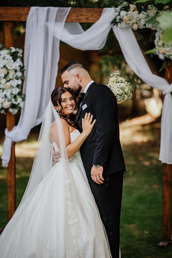 A romantic wedding ceremony moment with the couple sharing a tender kiss under a white draped outdoor gazebo.