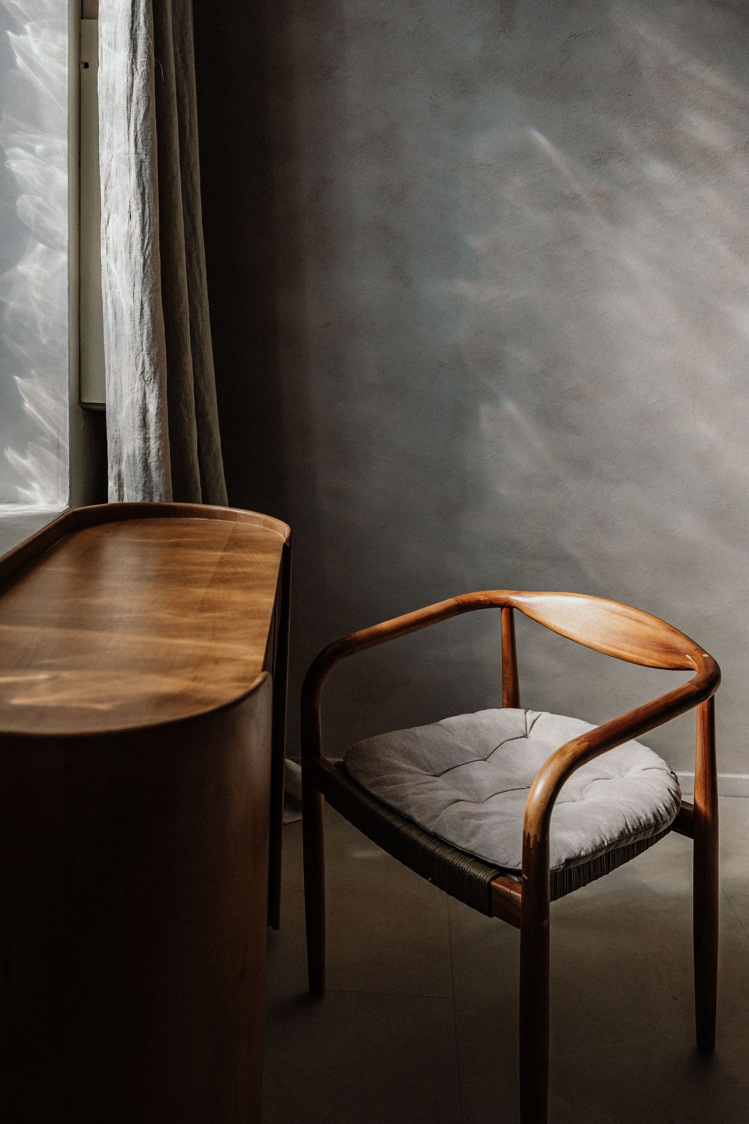 Modernes minimalistisches Interior mit rundem Holzstuhl & Kissen am Tisch am Fenster in stimmungsvollem Licht – Business Shooting Frankfurt
