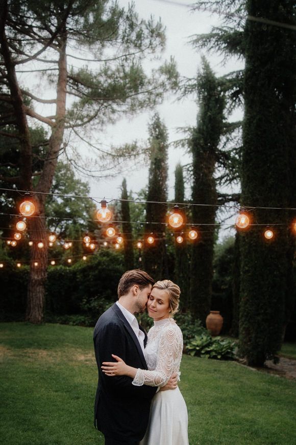 Abendliches Hochzeits­portrait unter Lichterketten mit Zypressen im Hintergrund – magische Momente beim heiraten im Morrhof.