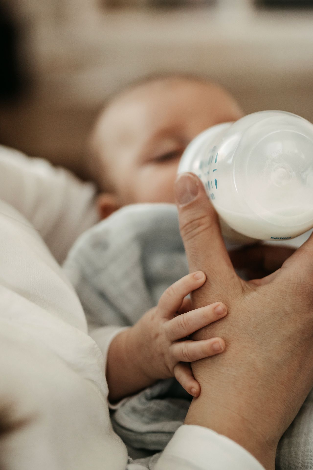 Close-up view of a baby bottle being held during feeding time against a soft gray background.