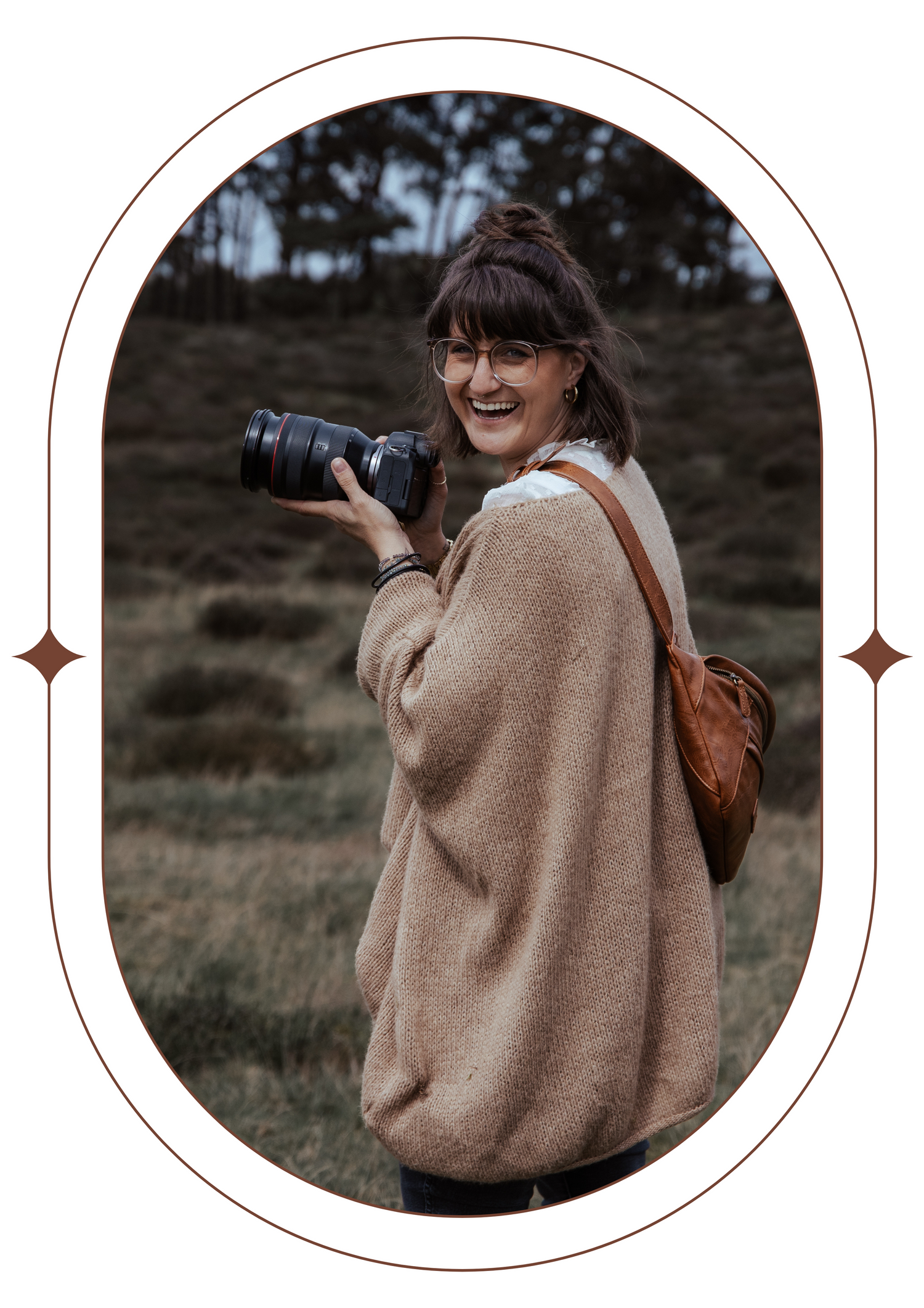 A photographer in warm winter attire poses with camera equipment against a natural backdrop.
