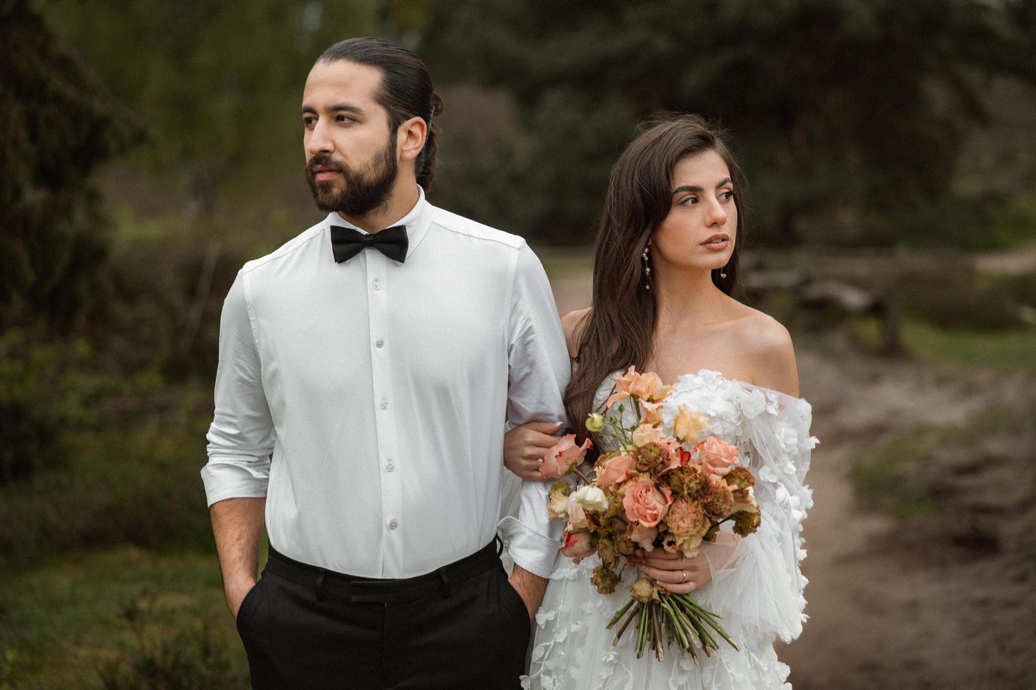 Elegant wedding couple in formal attire standing together on a nature path.