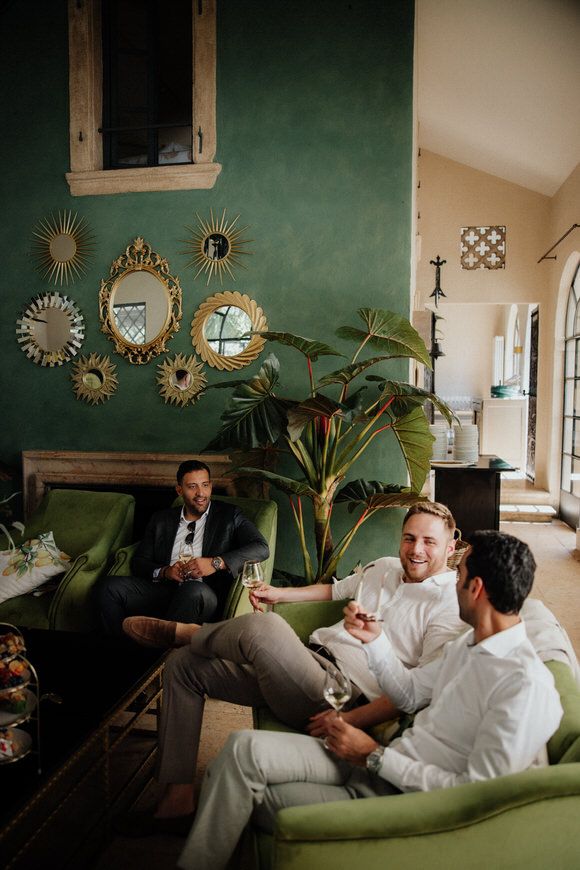 Trauzeugen entspannen mit Drinks auf einem grünen Samtsofa in elegantem Raum mit Sonnen­spiegeln – stilvoll heiraten im Morrhof.