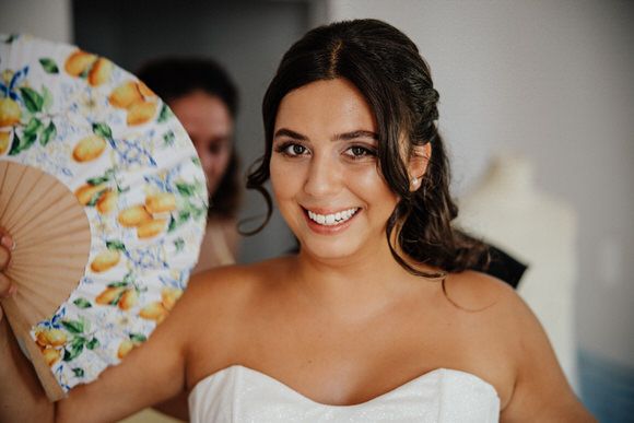 A person in a white strapless gown holds a decorative floral fan while posing for bridal portraits.