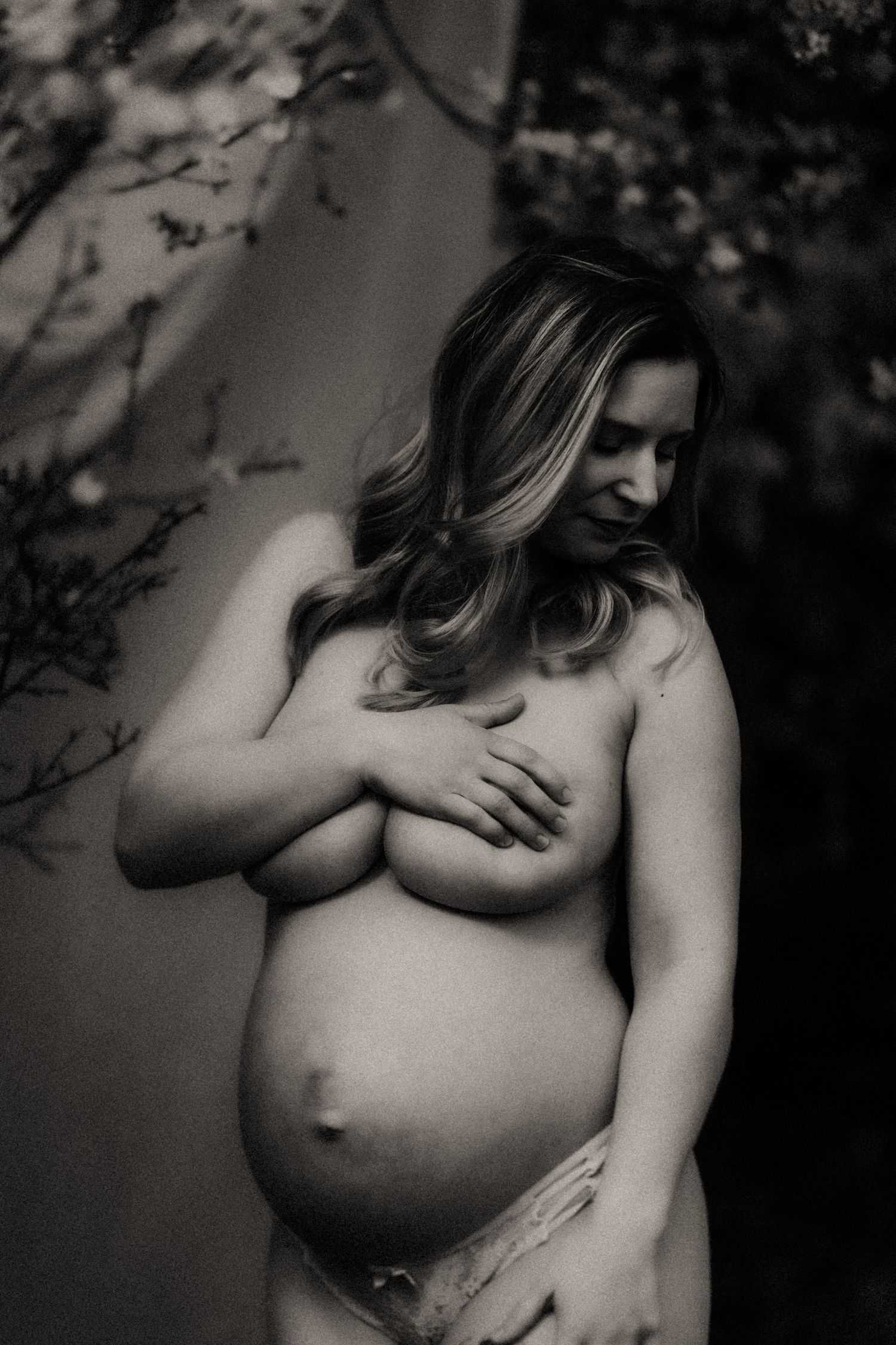 An artistic black and white maternity photograph showing a pregnant woman in a natural outdoor setting.