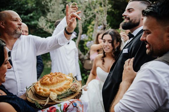 Hochzeitsfotograf Boudier & Koeller – Gäste lachen freudig beim Halten eines traditionellen Brotes im Freien.