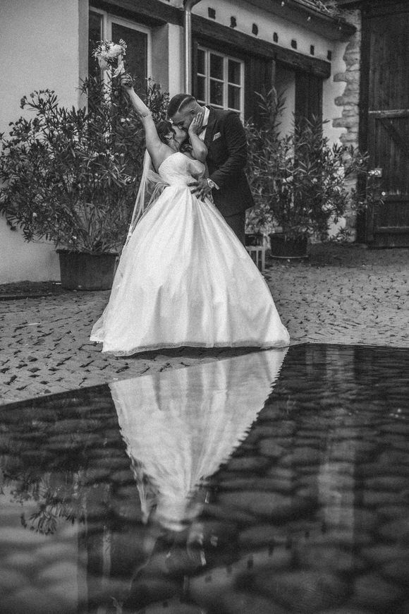 Hochzeitsfotograf Boudier & Koeller – Schwarz-Weiß-Serie: Braut im fließenden Kleid spiegelt sich auf Kopfsteinpflaster.