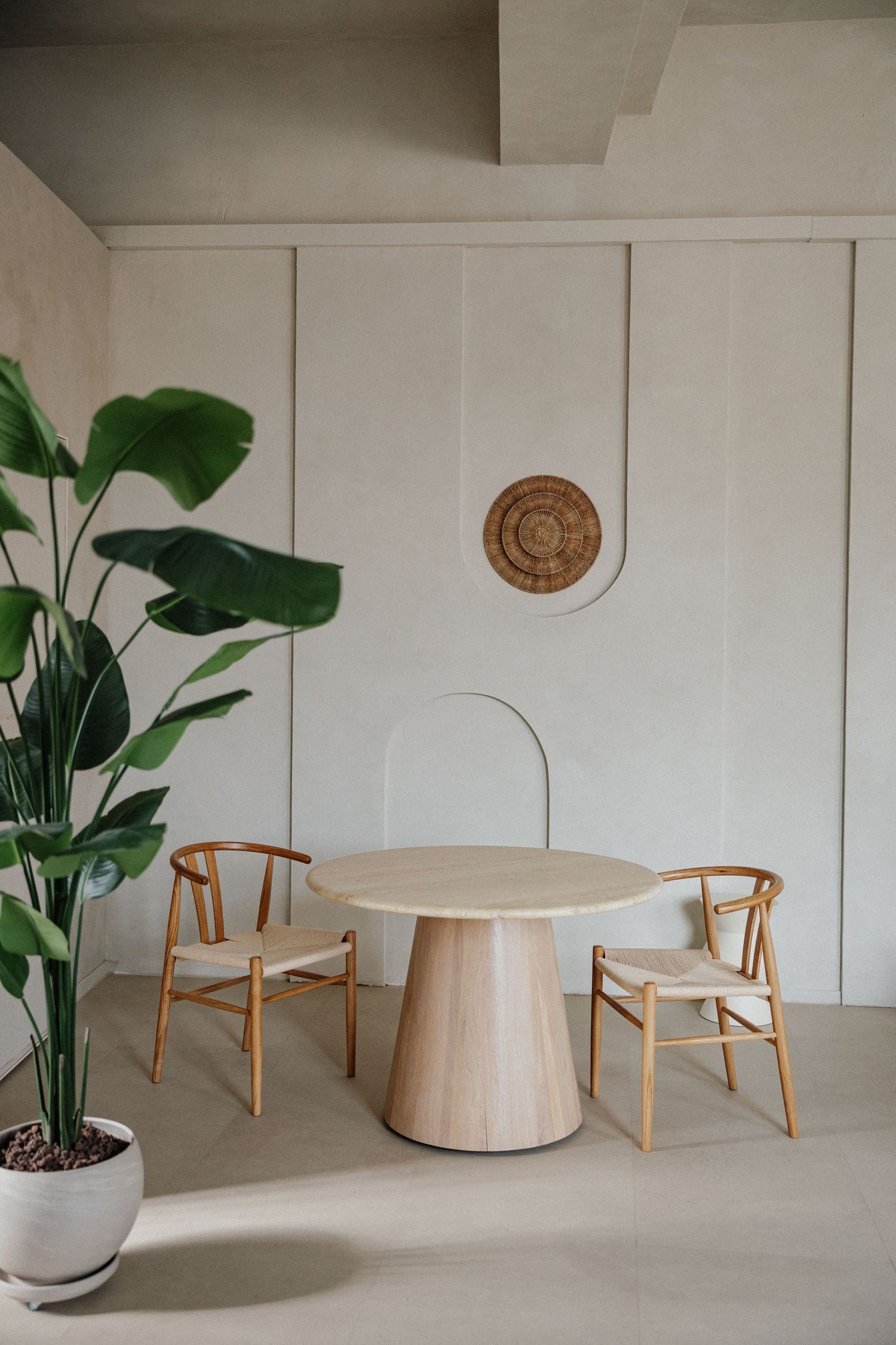 Modern-minimalistischer Essbereich mit rundem Cremetisch, Holzstühlen & großer Pflanze vor weißer Wand – Business Shooting Frankfurt