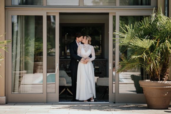Hochzeitspaar teilt einen intimen Moment vor moderner Architektur mit Palmen – stilvoll heiraten im Morrhof.