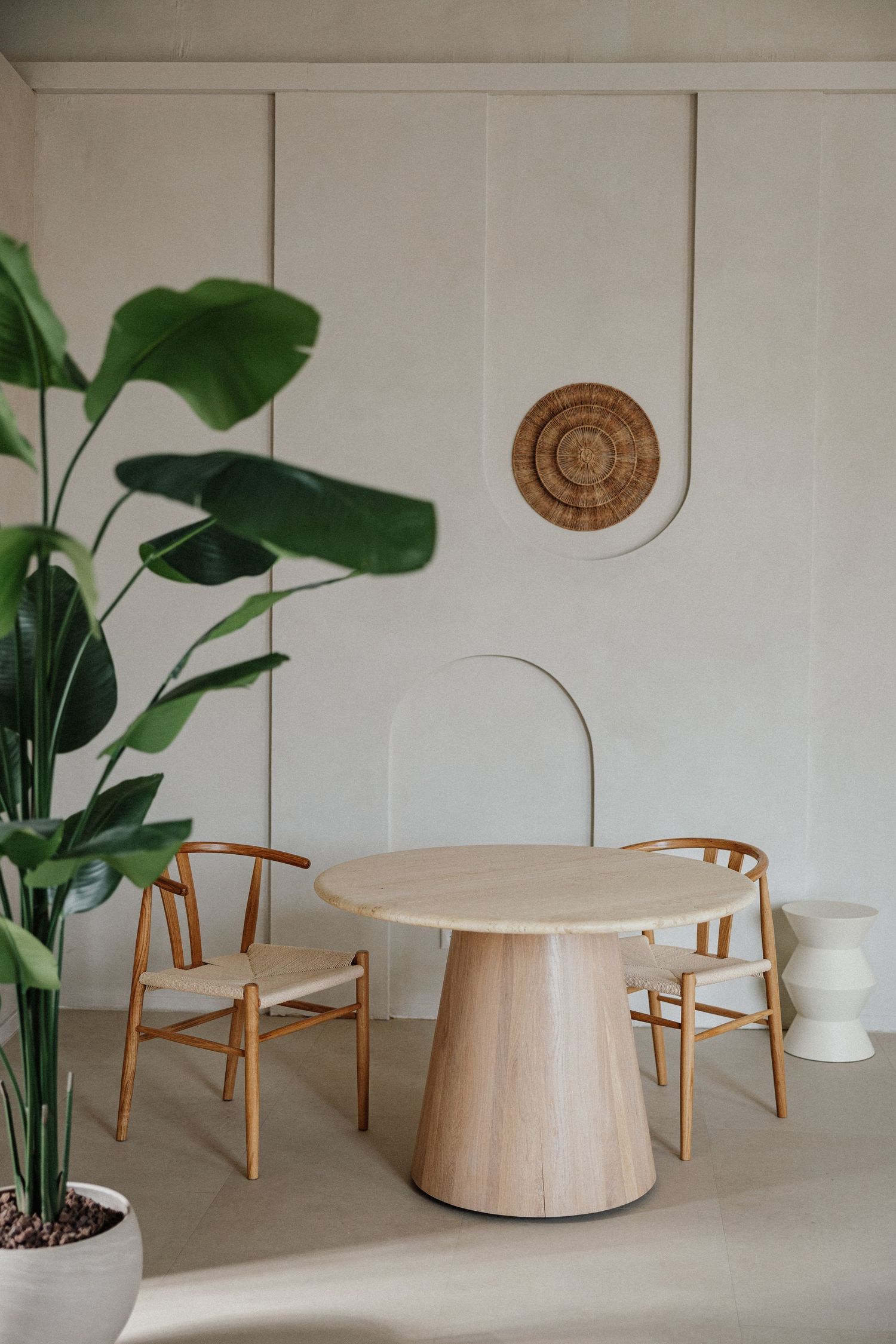 Moderner Essbereich mit rundem Holztisch, Wishbone-Stühlen & großer Pflanze vor weißer Wand mit runder Deko – Business Shooting Frankfurt