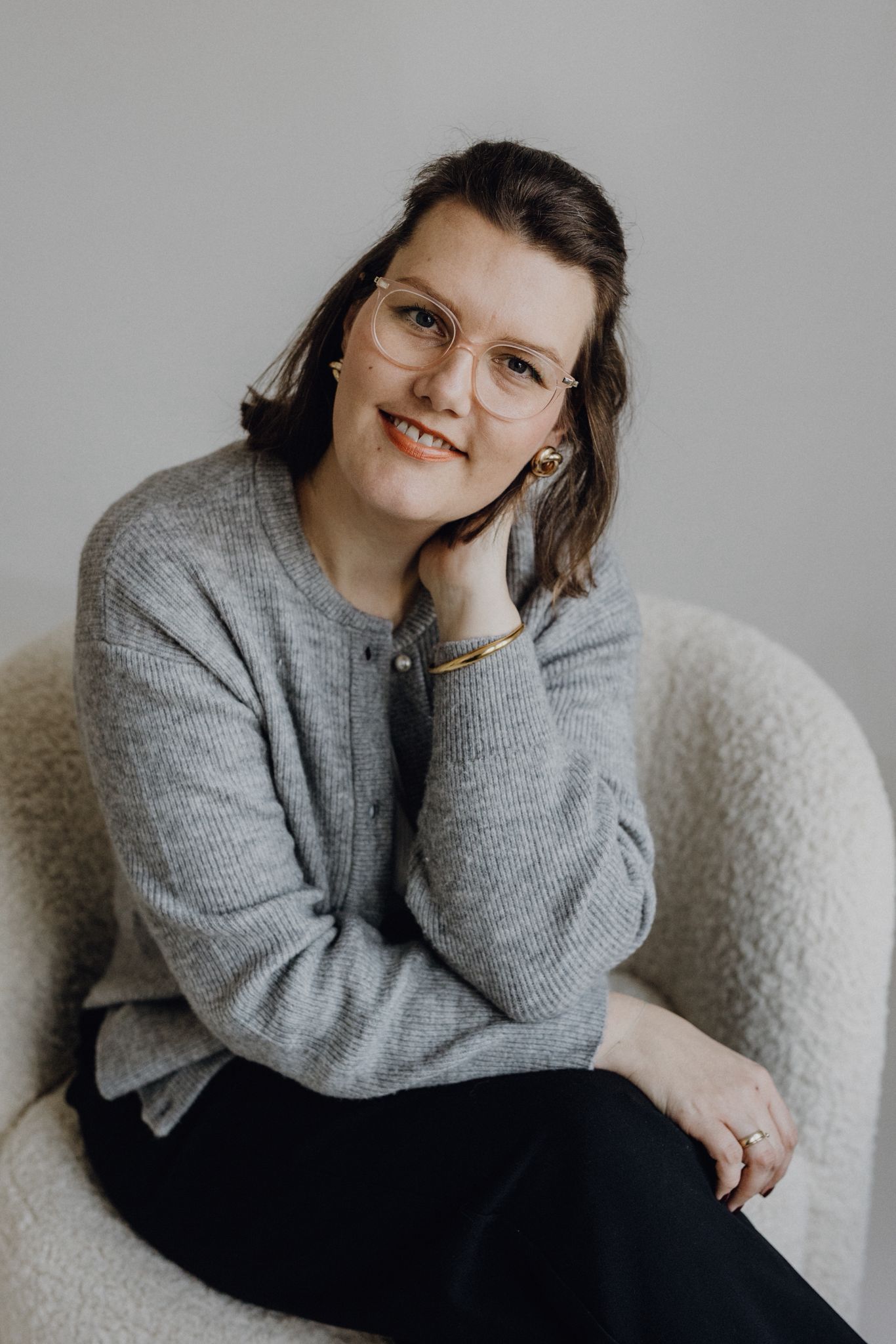 A person wearing a cozy gray sweater poses against a light background in a minimalist portrait series.