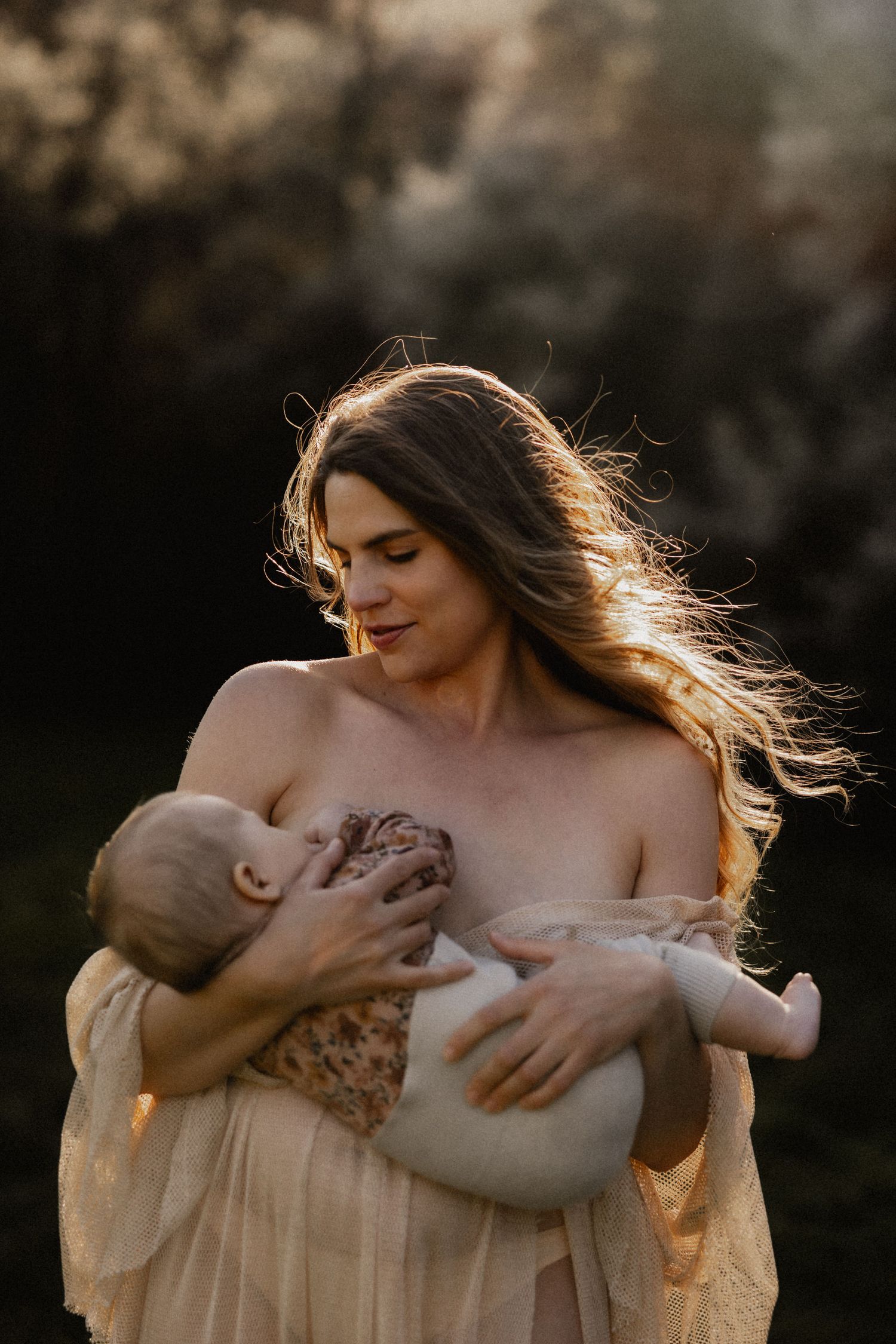Mother and baby share an intimate bonding moment in golden sunlight during outdoor photography session.