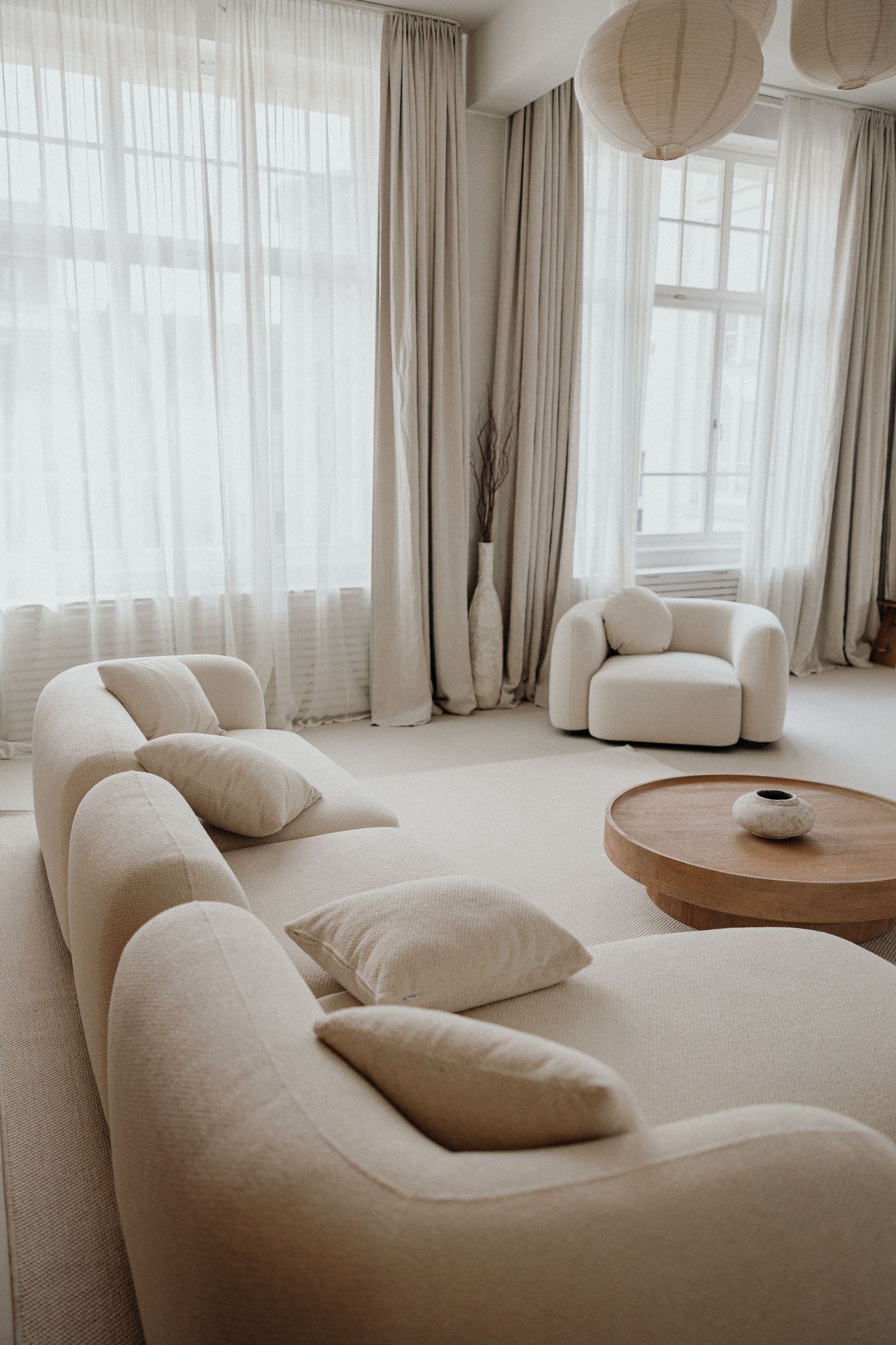 Modernes minimalistisches Wohnzimmer mit beige-rundem Ecksofa, weißen Papierlampen & lichtdurchlässigen Vorhängen – Business Shooting FFM