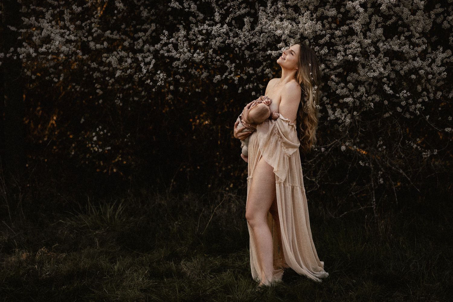 A person in a flowing beige dress poses against a dark background with blooming spring flowers.
