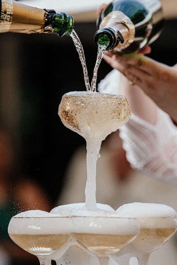 Champagner wird in einen Turm aus Vintage-Coupe-Gläsern gegossen – festlich heiraten im Morrhof.