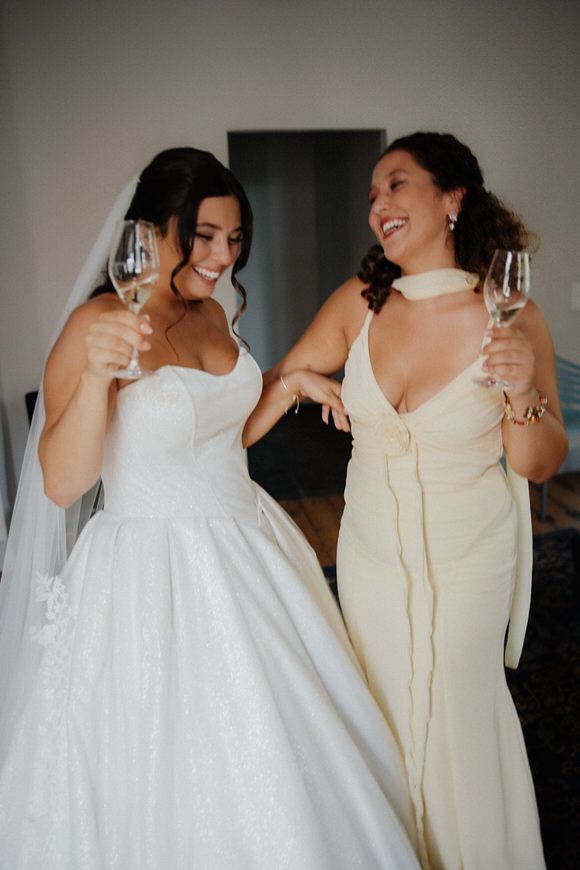 Two people in formal attire share a joyful moment while holding champagne glasses during a wedding celebration.