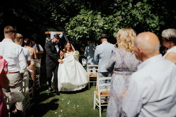 Outdoor garden wedding reception with guests mingling under trees and white table settings.