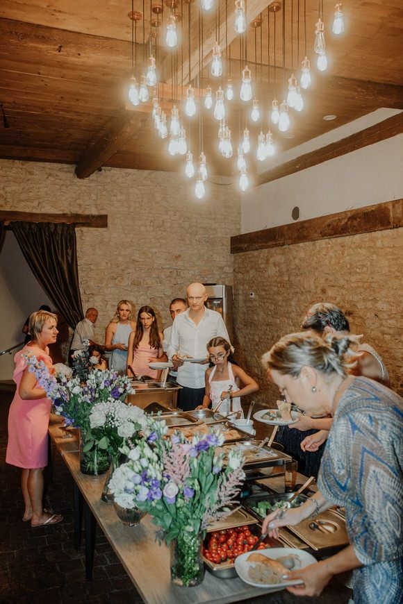Hochzeitsfotograf Boudier & Koeller – Gäste am Buffet unter Holzbalken und Edison-Lampen in eleganter Location.