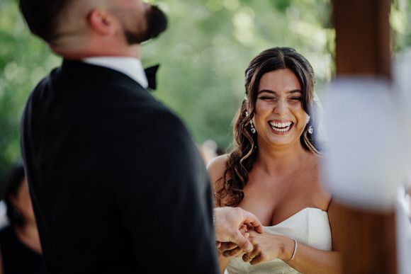 A joyful bride in a strapless white dress laughs during an outdoor wedding ceremony.
