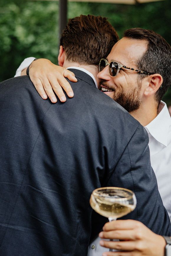 Freunde umarmen sich und halten Champagnergläser bei einer Feier im Freien – gemeinsam heiraten im Morrhof feiern.
