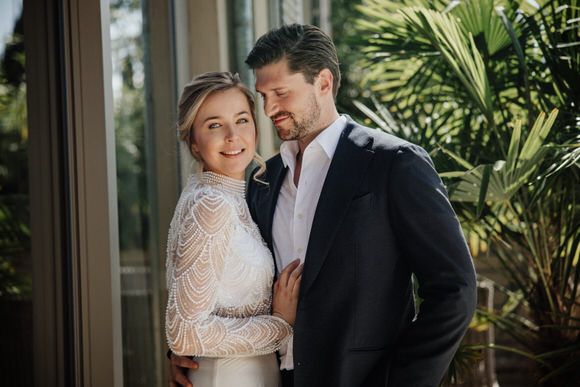 Elegantes Brautpaar posiert vor tropischem Grün und Glasfassade – modern heiraten im Morrhof.