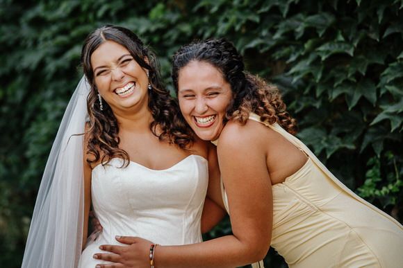Two people sharing joyful laughter together while posing outdoors with greenery in the background.
