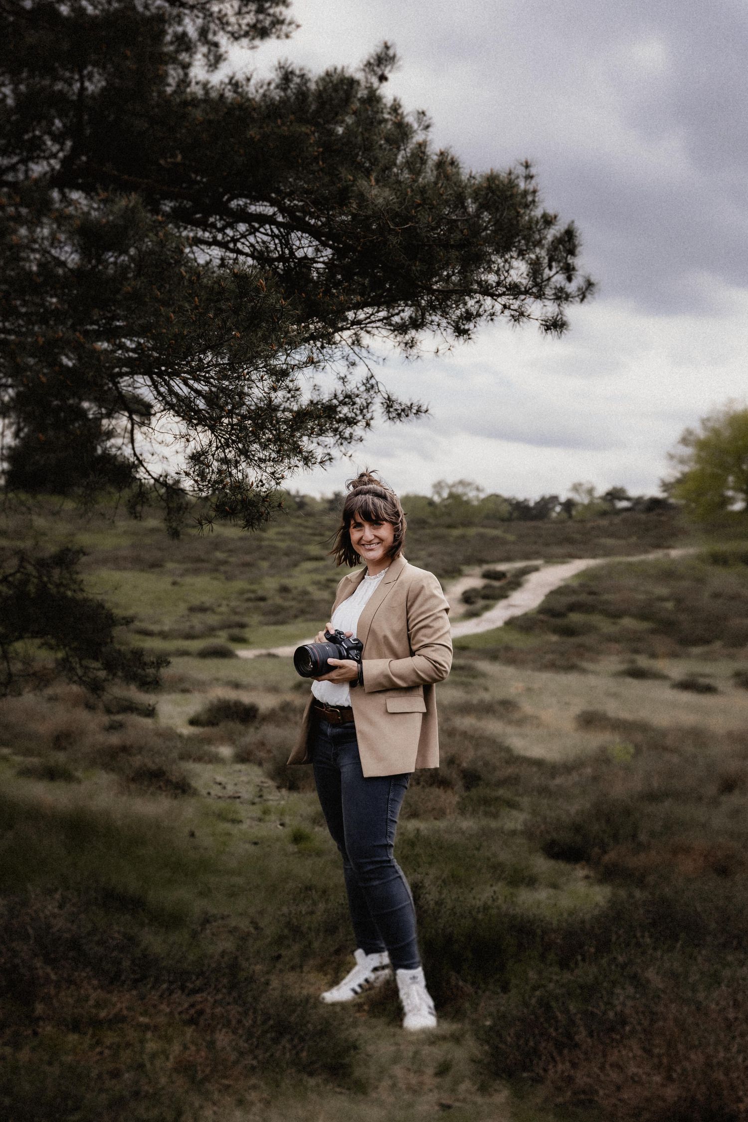 A photographer with a vintage camera explores a misty heathland landscape under moody cloudy skies.
